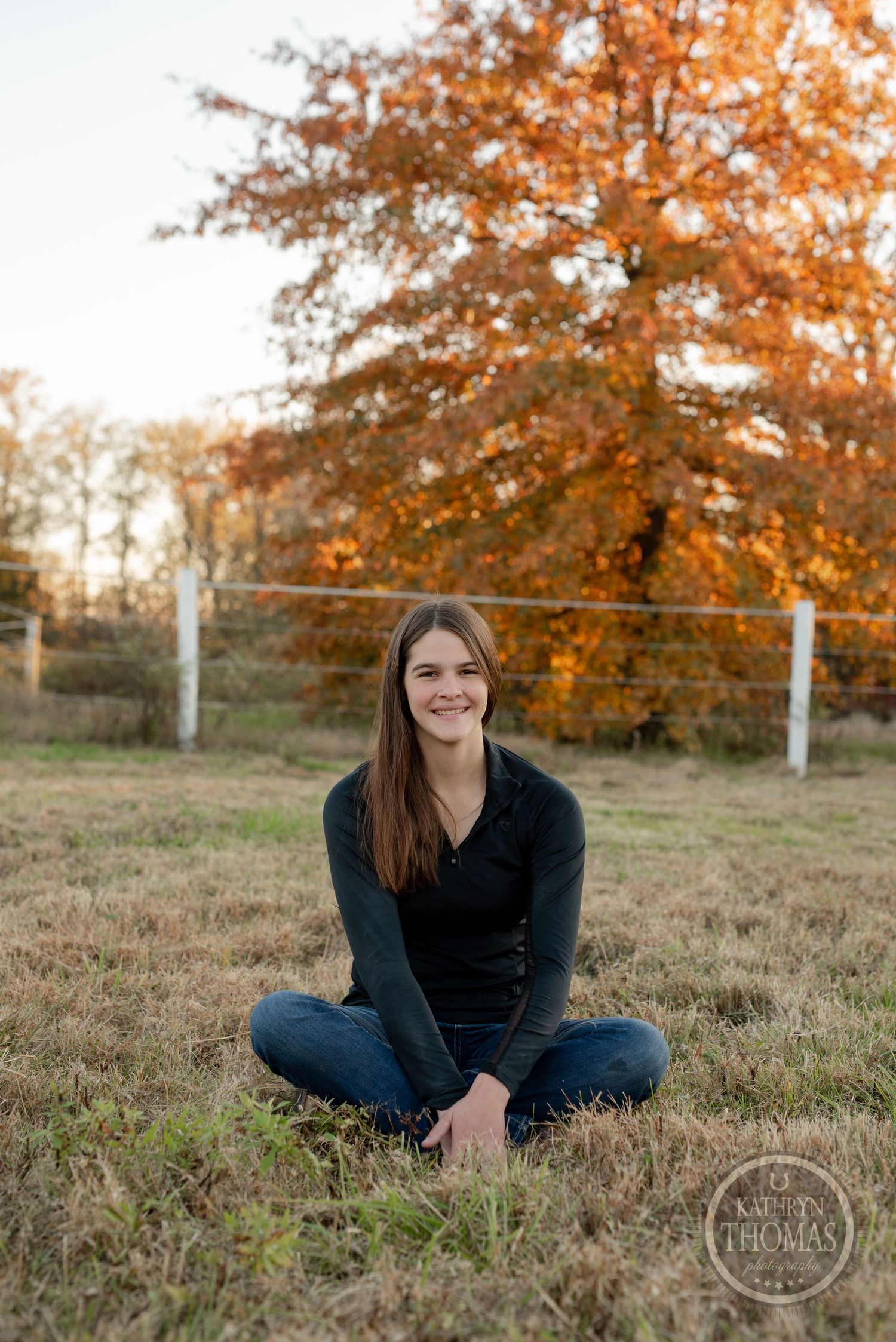 Outdoor fall portrait with vibrant orange trees and rustic farm elements.