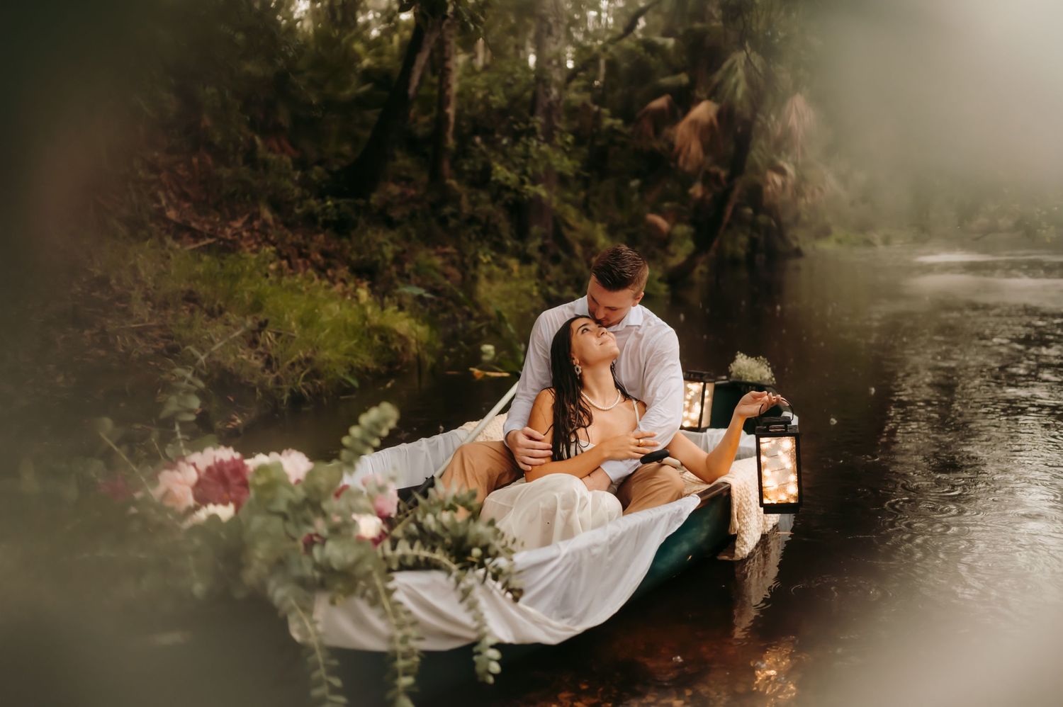 Man and woman sitting in a row boat on the water, with beautiful lush green foliage surrounding them.