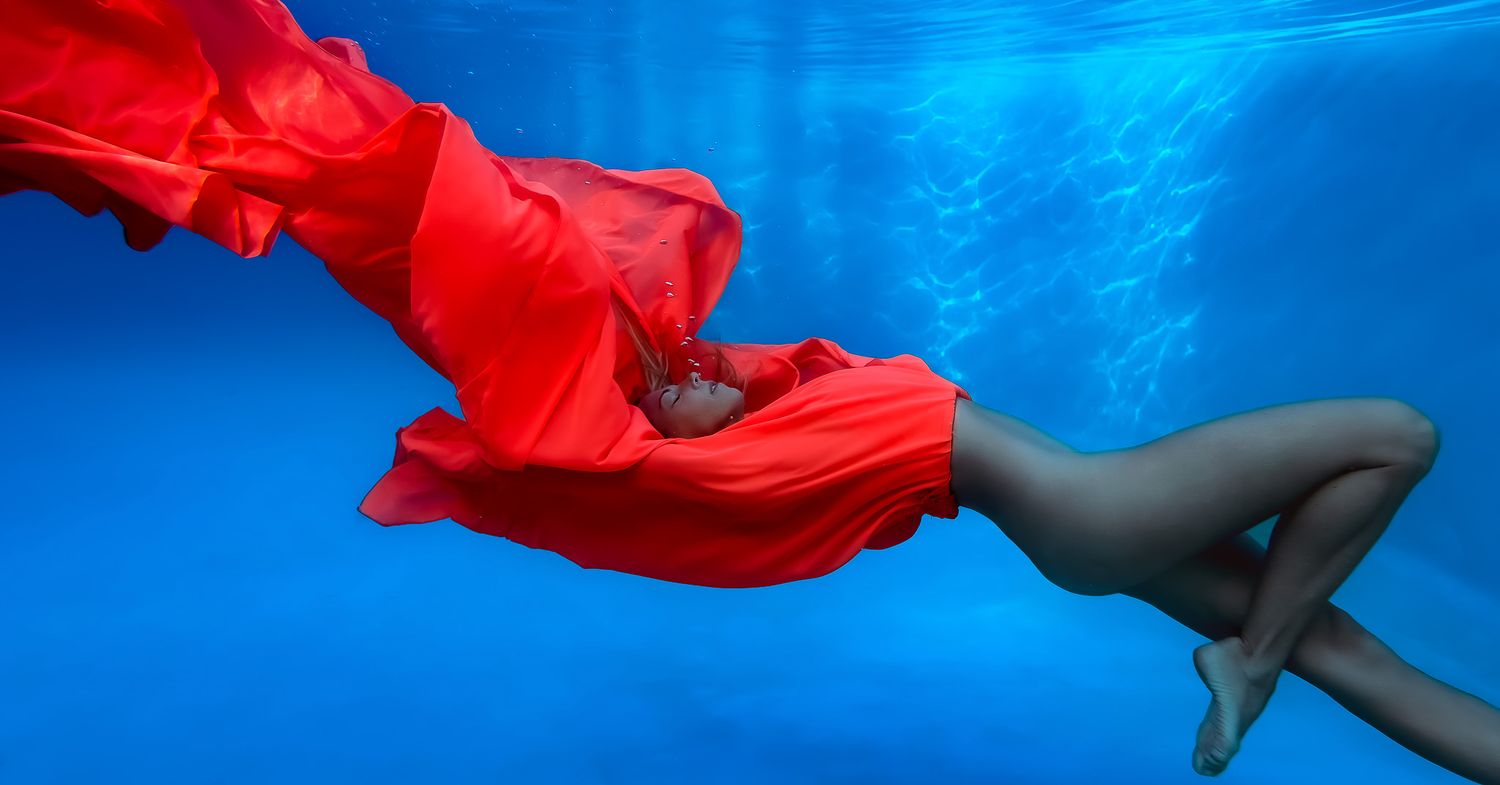 Artistic underwater photo with flowing red fabric against deep blue background.