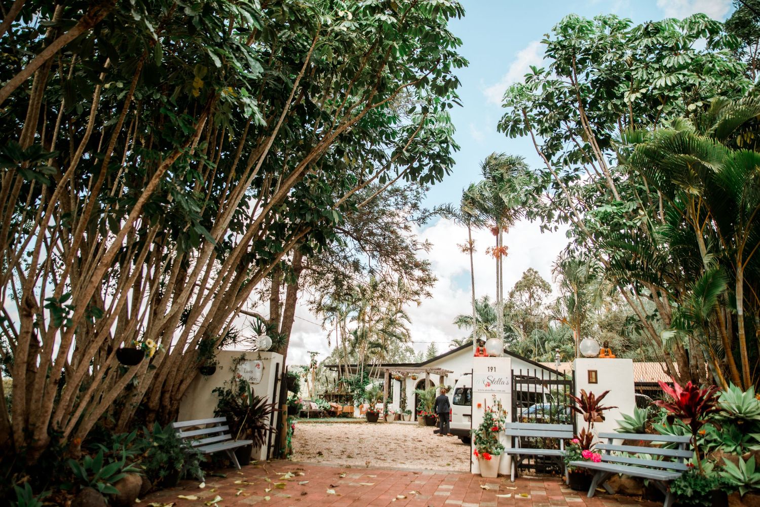 Garden pathway lined with trees and tropical plants leading to an outdoor venue.
