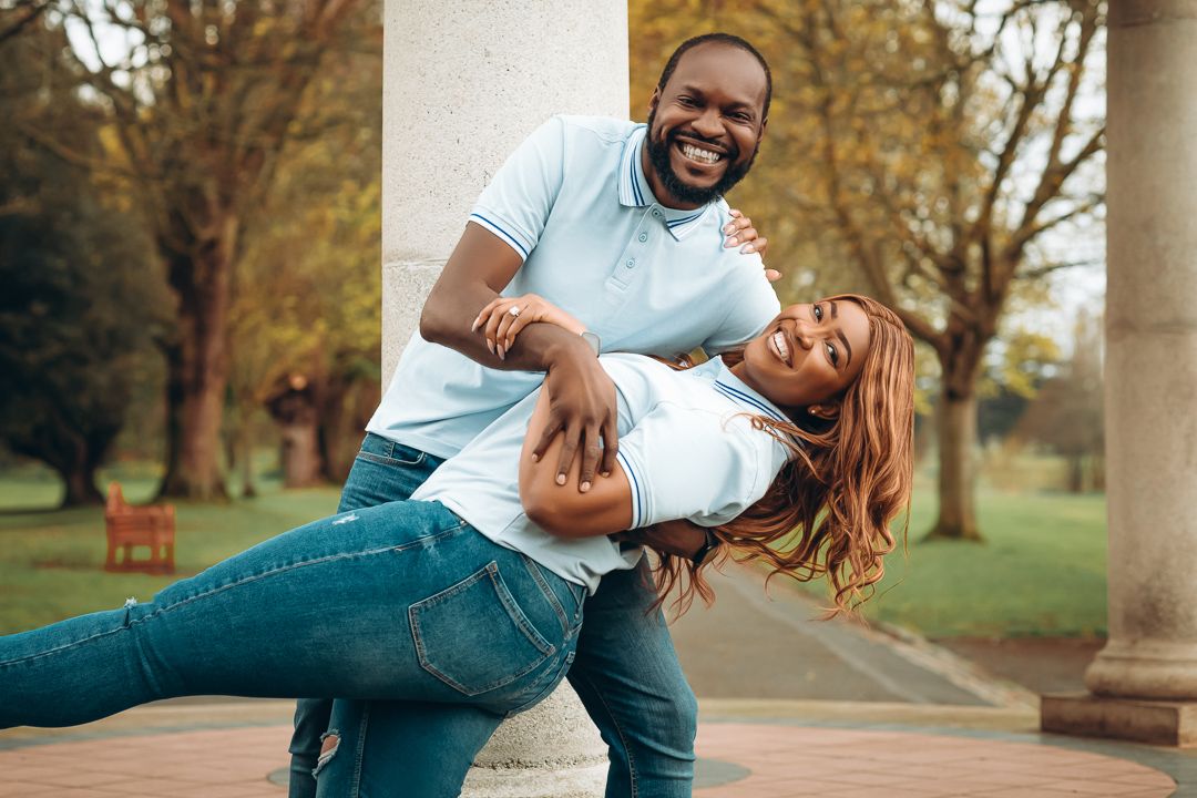 Playful couple dances and poses in casual wear at outdoor park setting.
