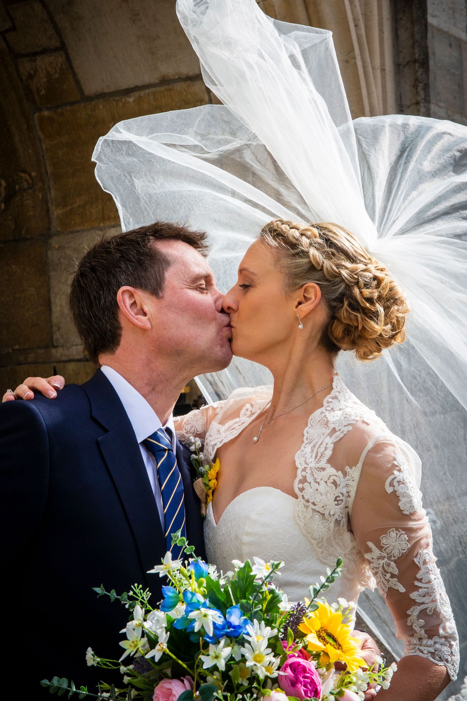 A romantic wedding moment captured as newlyweds kiss under a flowing veil.