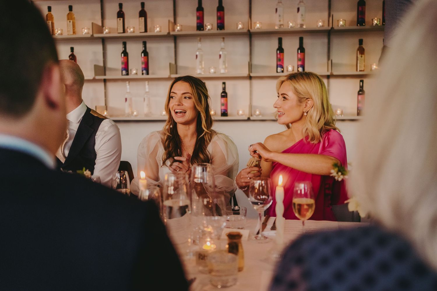 Wedding guests enjoying drinks and conversation in an upscale restaurant with bottle-lined walls.