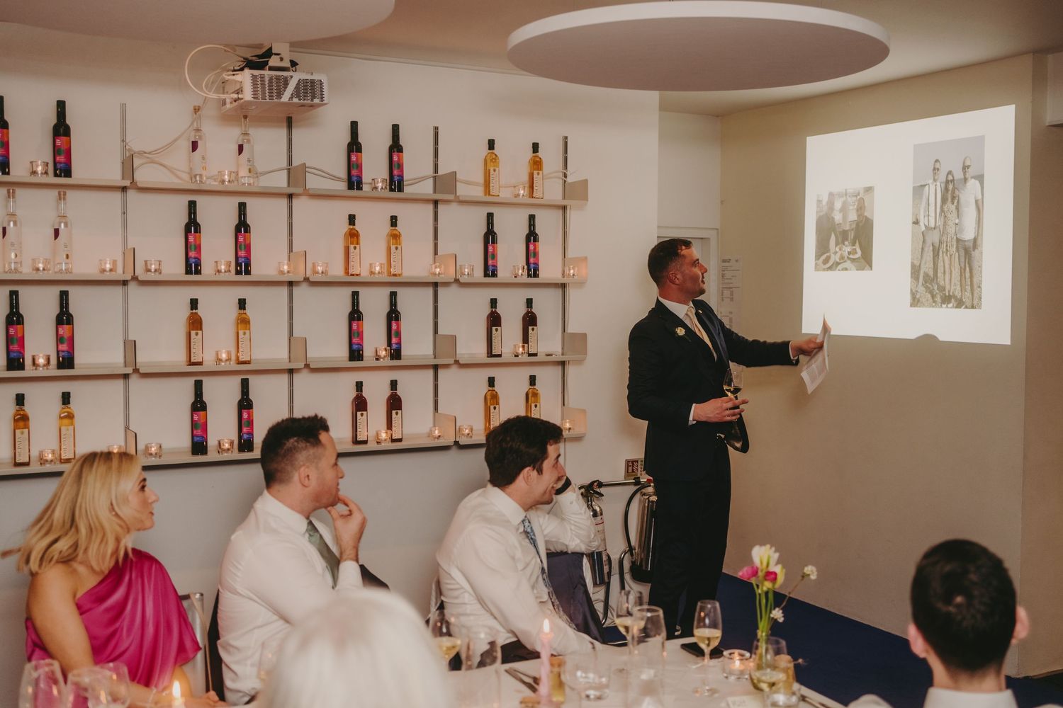 Wedding reception speech being given while guests watch a projected presentation.