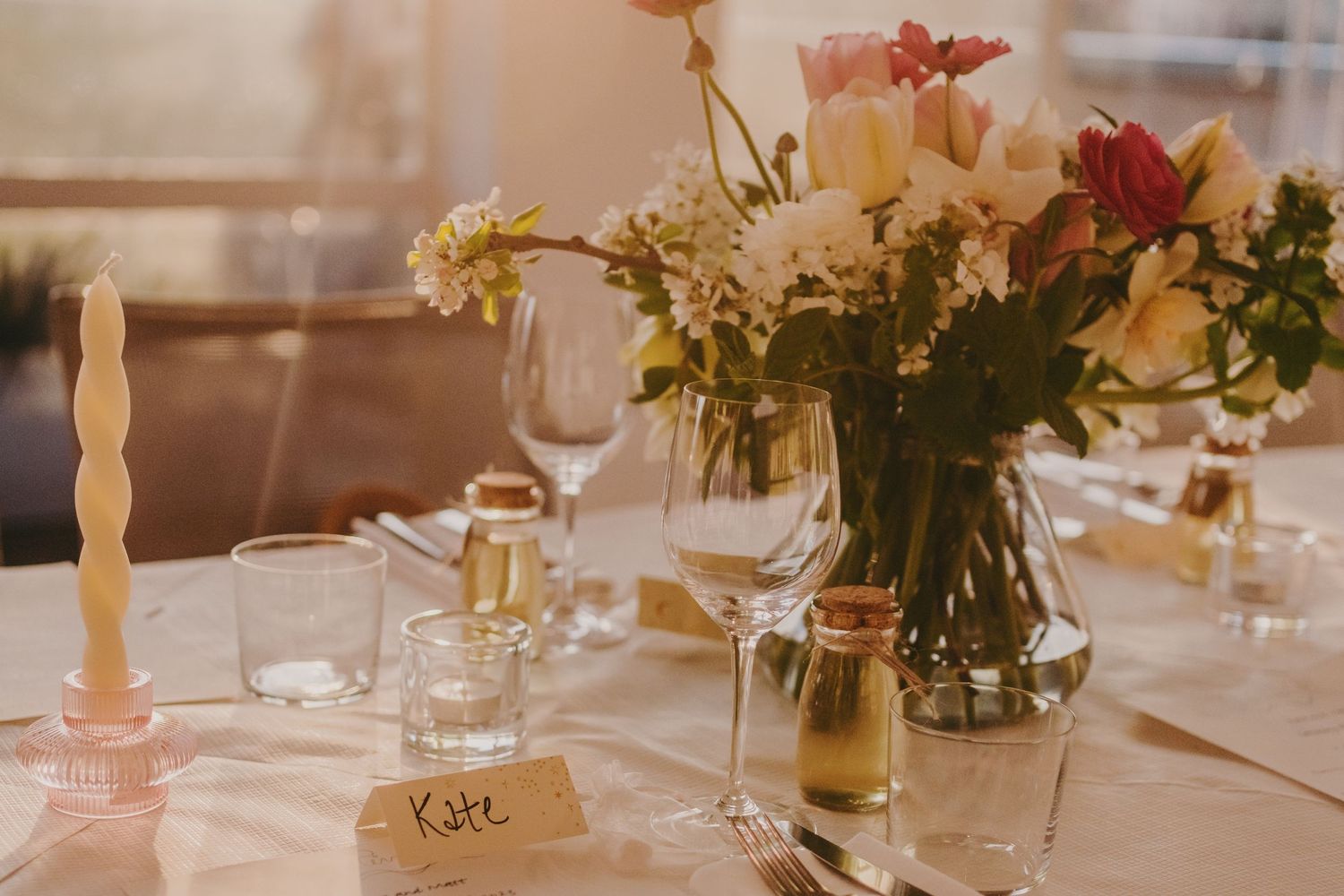 Elegant wedding table setting with floral centerpiece, candles, and wine glasses on white tablecloth.