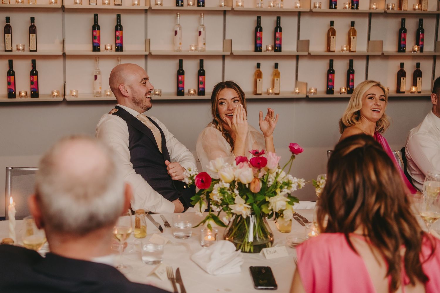 Lively wedding reception scene with guests laughing during dinner and speeches.