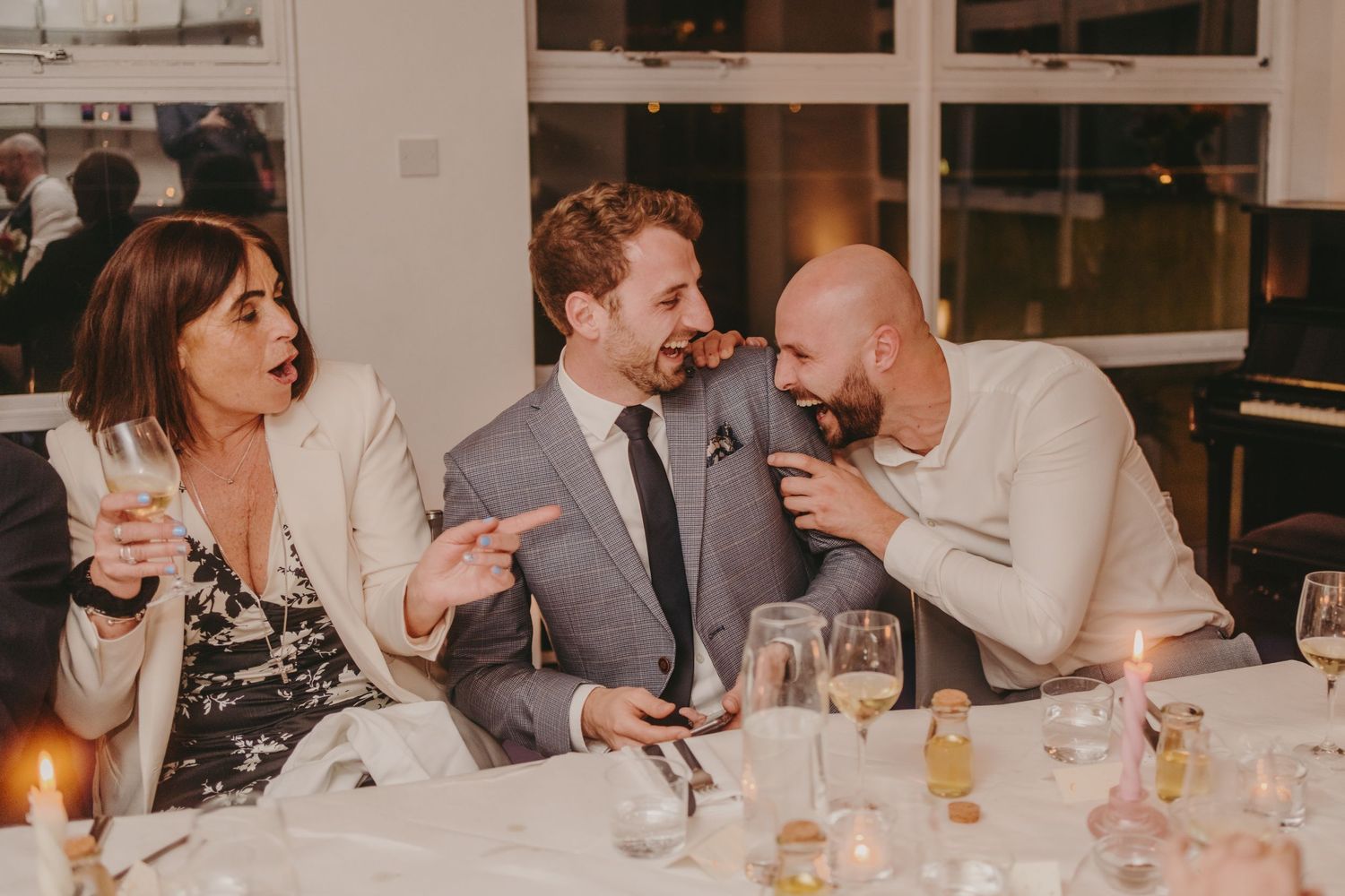 Dinner guests laugh joyfully together at an elegant restaurant table with wine glasses and candles.