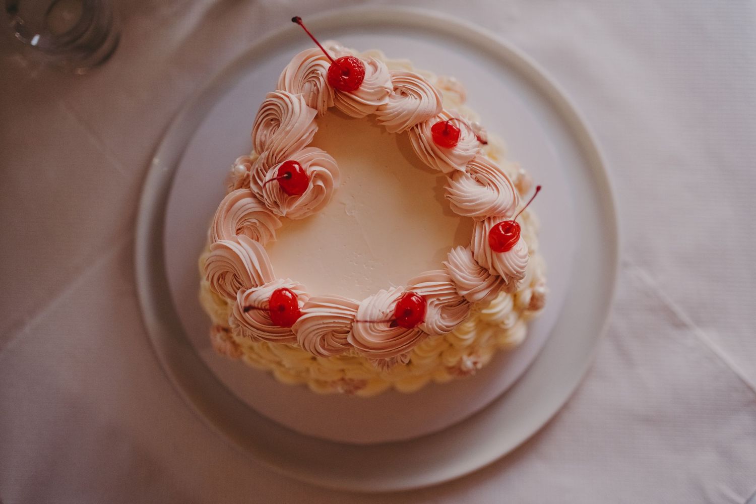 Close-up of white frosted cake with red cherries arranged in decorative pattern.