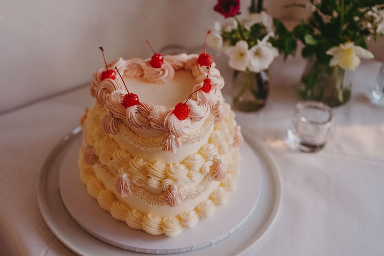 Two-tiered white wedding cake decorated with whipped cream and red cherries on top.