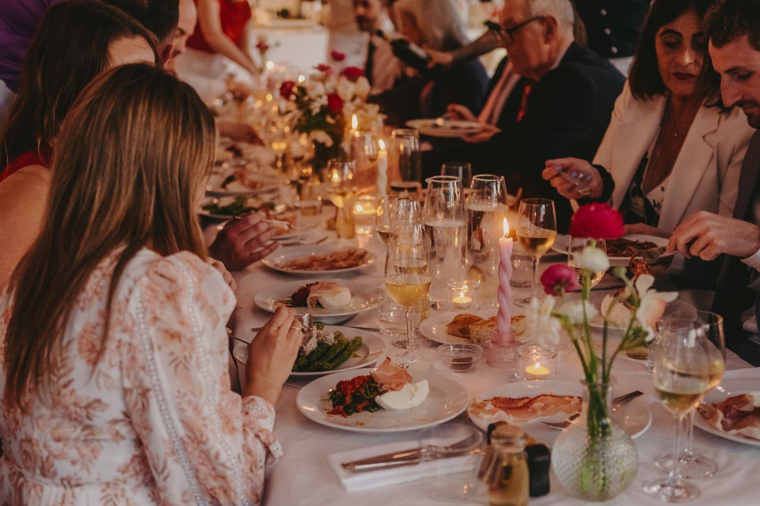 Wedding reception dinner table set with candles and floral arrangements as guests dine.