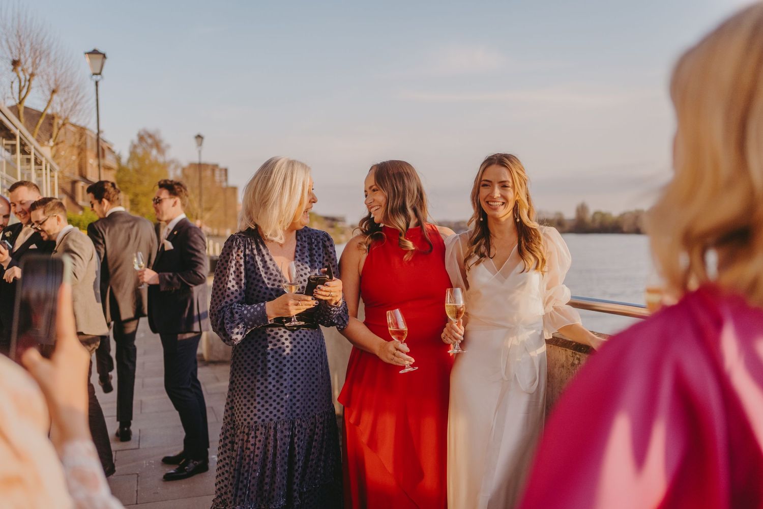 Guests mingling at an outdoor waterfront reception during golden hour.