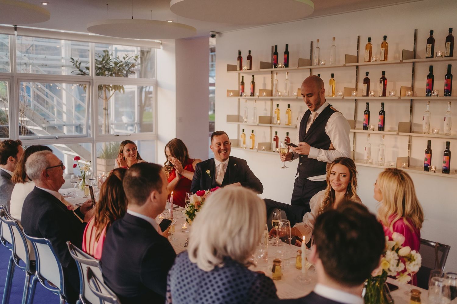 Dining room with modern decor featuring floor-to-ceiling windows and bottle display shelves.