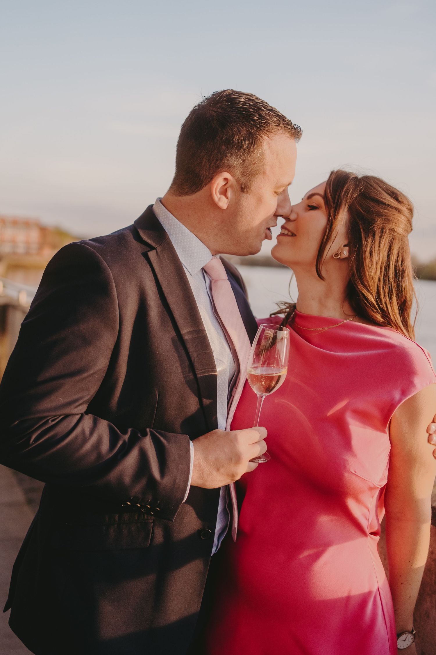 A couple shares an intimate moment while holding champagne glasses against a sunset backdrop.