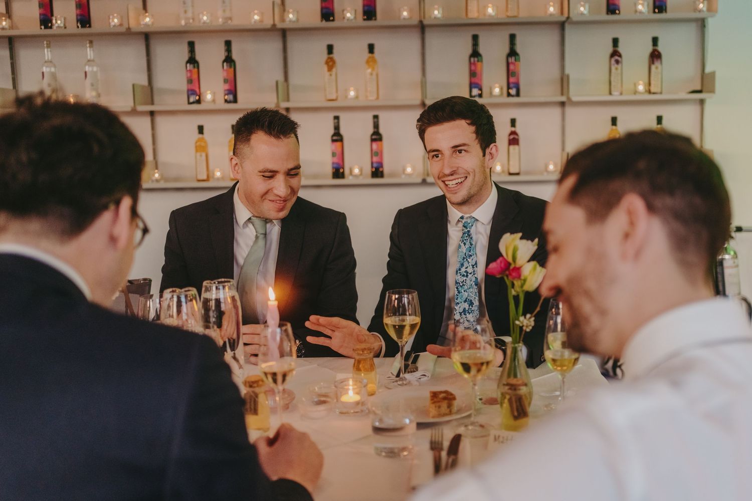 Groomsmen sharing drinks and conversation at wedding reception dinner table.