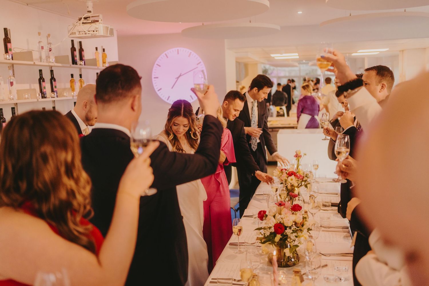 Wedding reception dinner in a modern venue with pink lighting and floral centerpieces.
