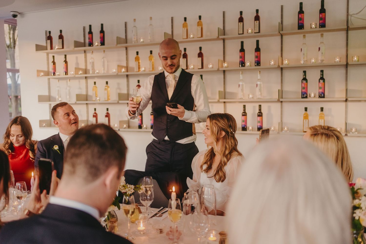 Event space with elegant table settings and wall-mounted wine bottle display shelves.