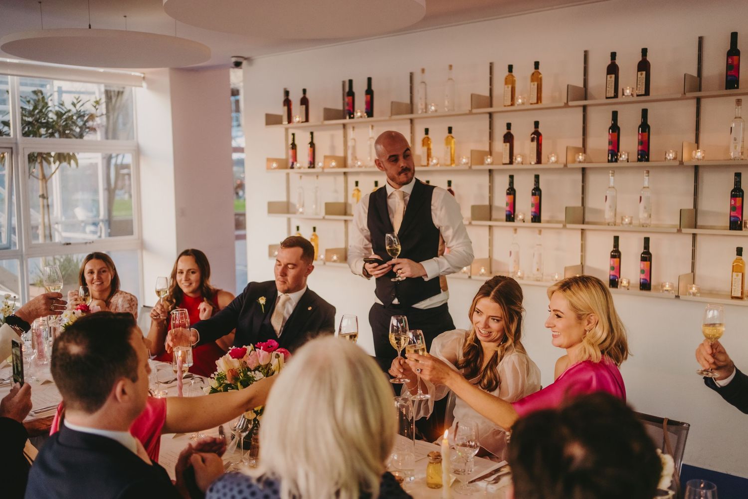 Restaurant server interacts with wedding guests seated at tables with pink floral arrangements.
