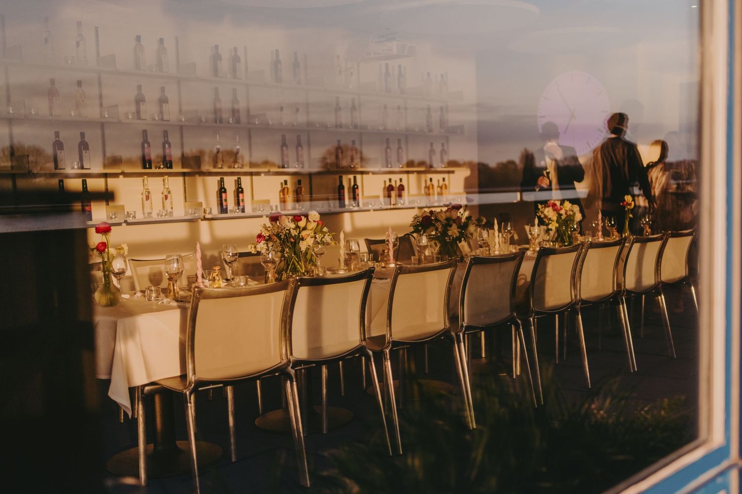 Long elegant table setting with white linens and floral arrangements against a sunset backdrop.