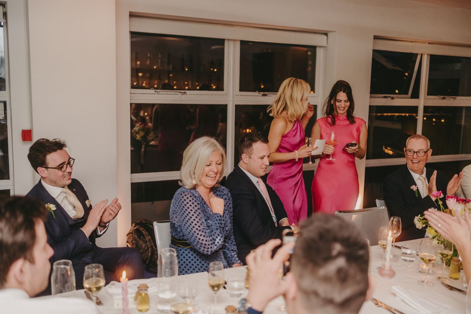 Wedding guests applauding during reception speeches at an elegant dinner venue.