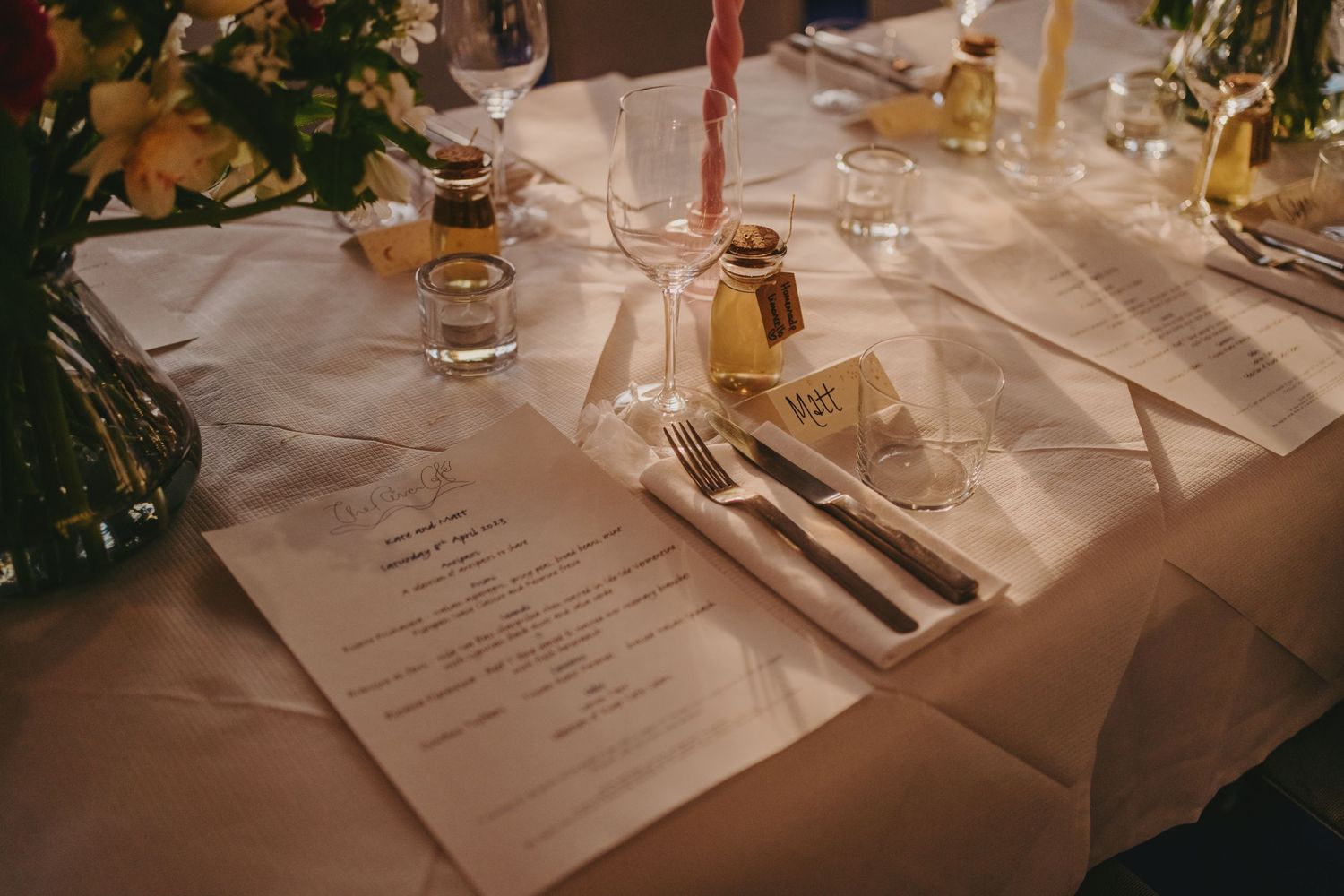 A formal dining table setup with menus, silverware, and romantic candlelight.