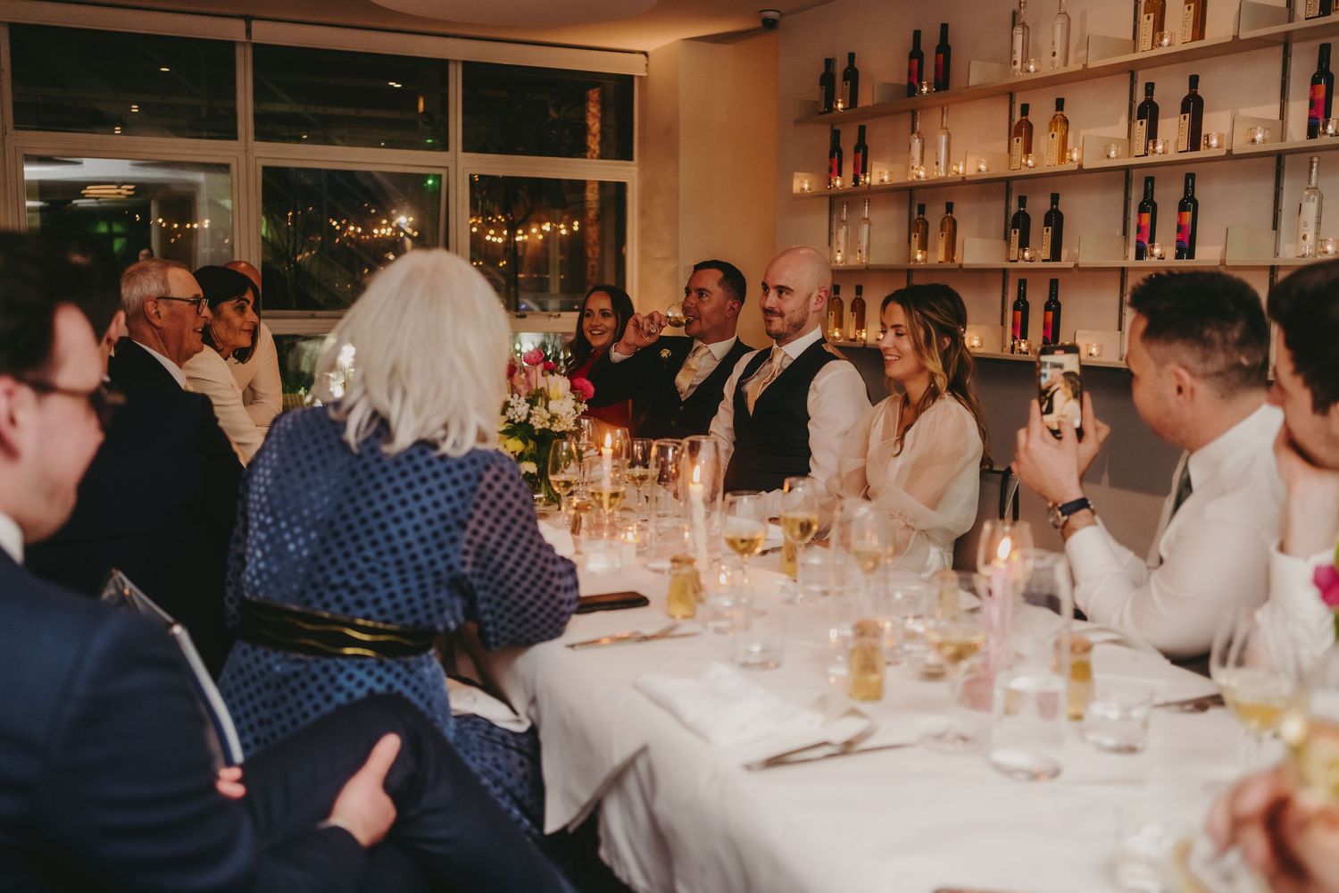Intimate wedding reception dinner with guests seated around a long white-clothed table.