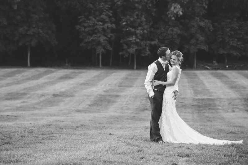 Black and white portrait of newlyweds embracing on a manicured lawn.