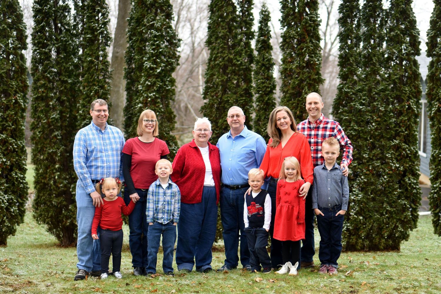 Large family group poses for a portrait in front of tall evergreen trees.