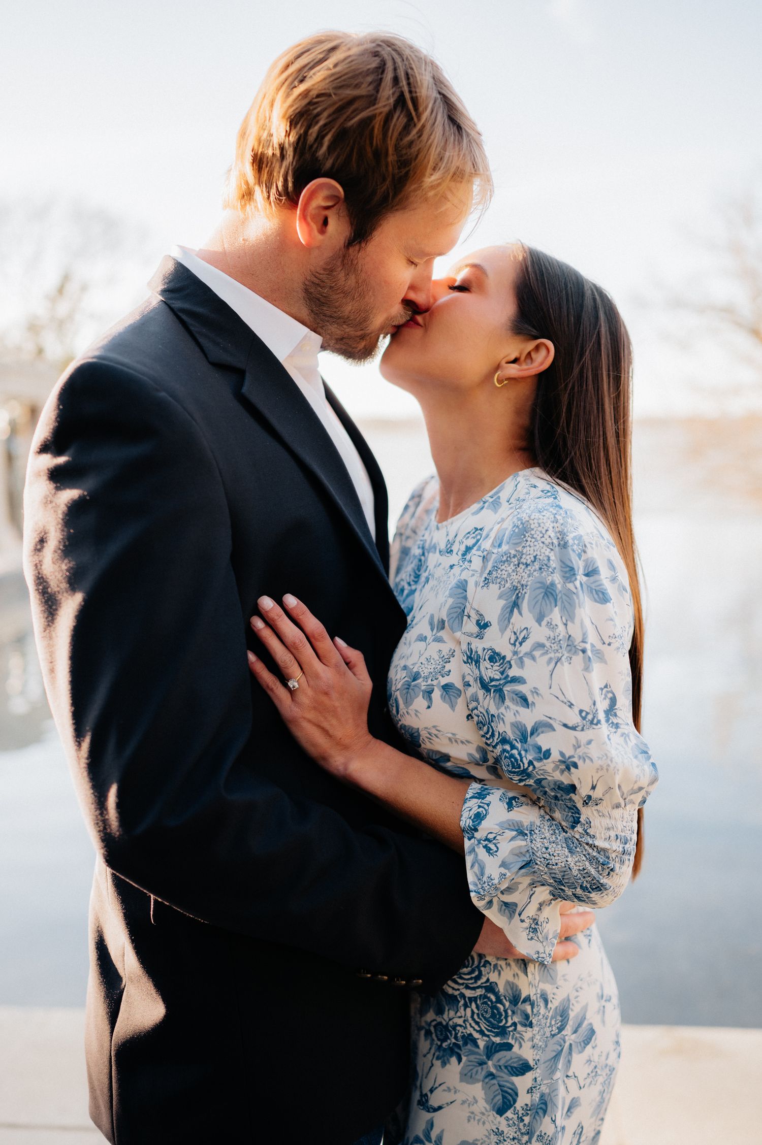 Couple in formal wear sharing tender kiss during outdoor photoshoot.