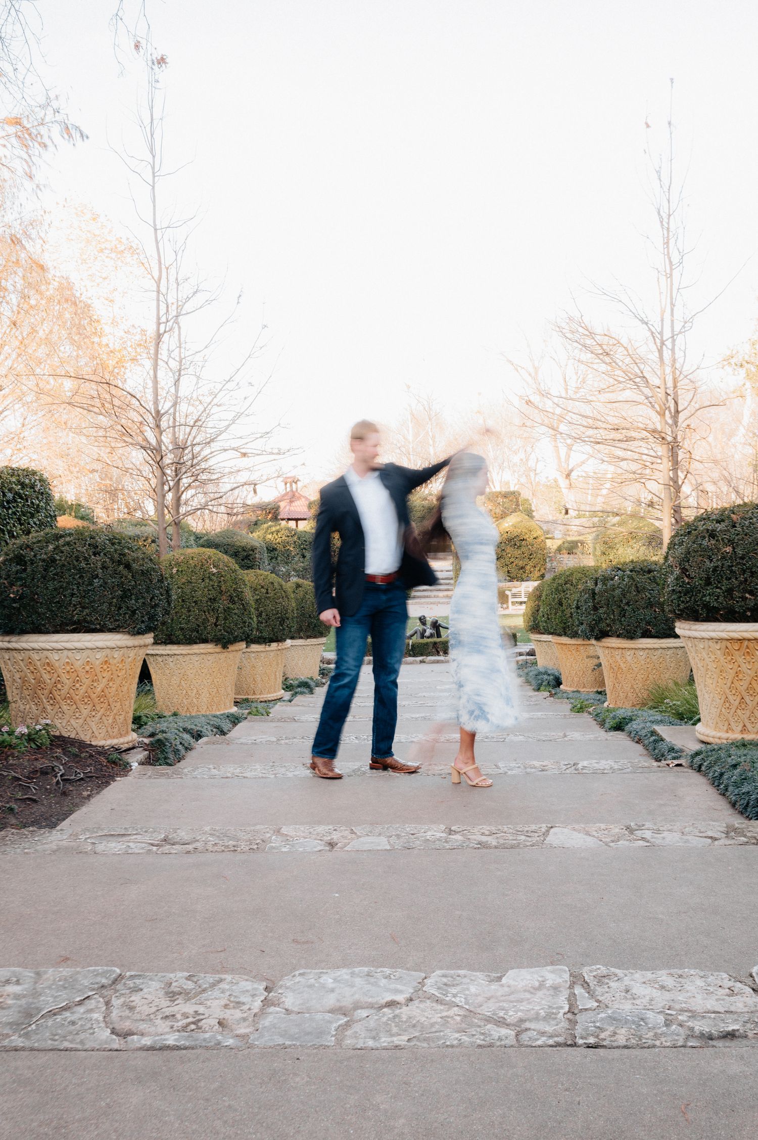 Romantic couple dancing on garden path surrounded by manicured hedges and planters.