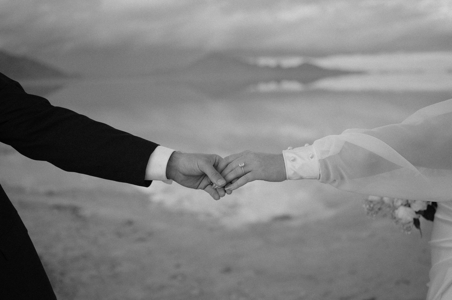 Black and white close-up of couple holding hands during wedding ceremony.