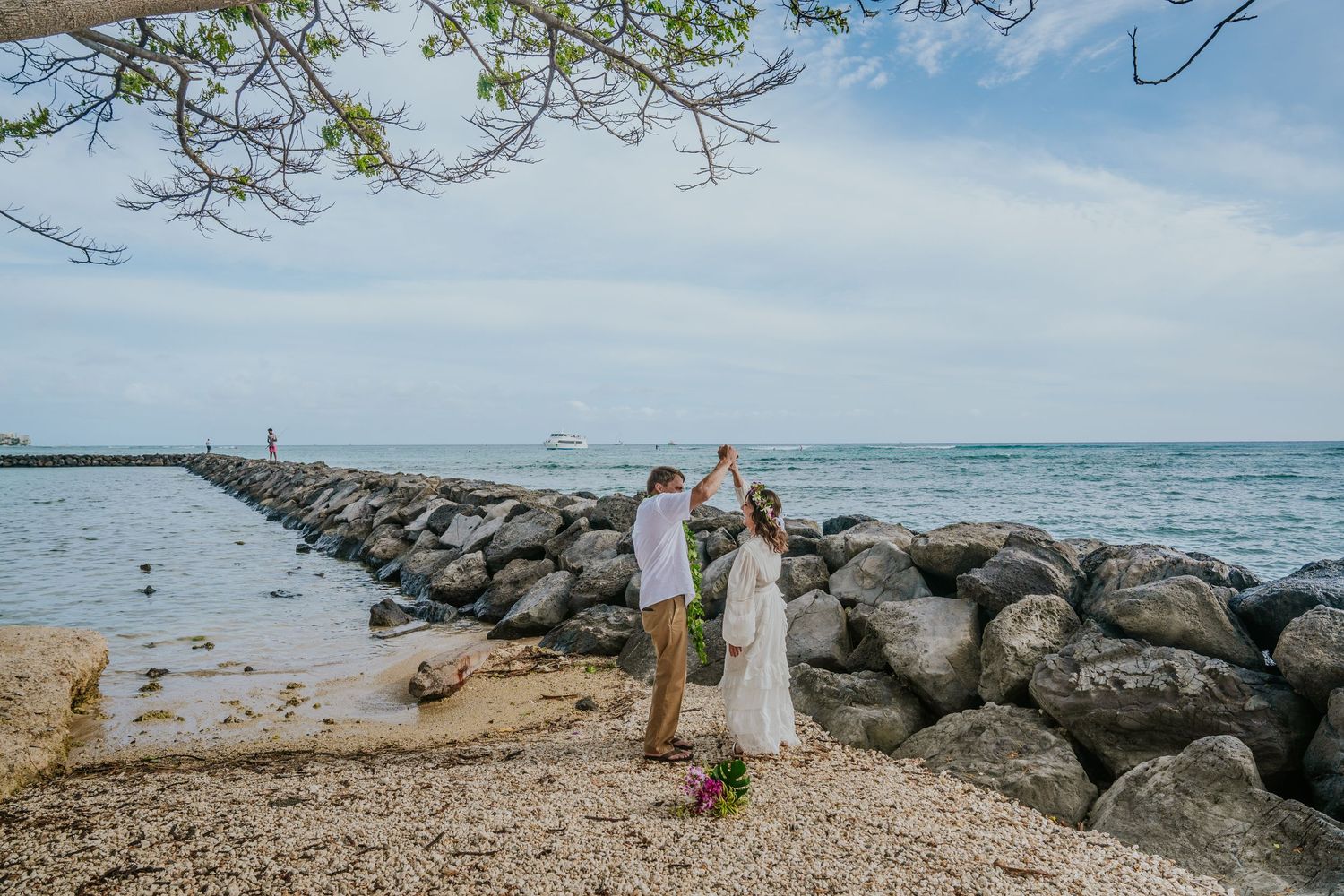 Wedding celebration on a rocky beach pier with ocean and cloudy sky backdrop.
