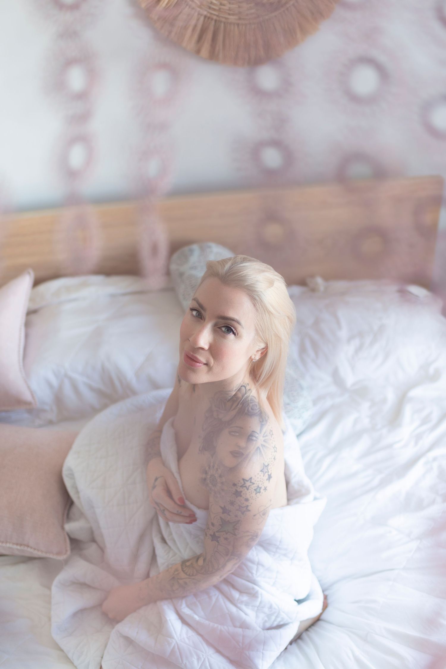 Dreamy boudoir photo of woman wrapped in white sheets on bed with decorative ceiling.