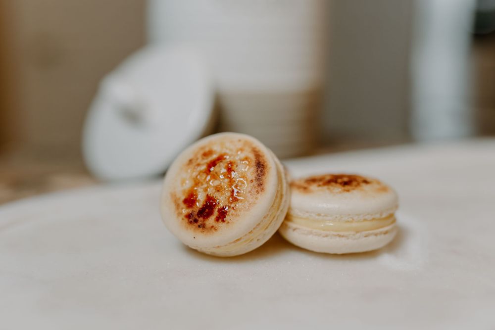 Close up of pale pink macarons with caramelized topping on a white surface.