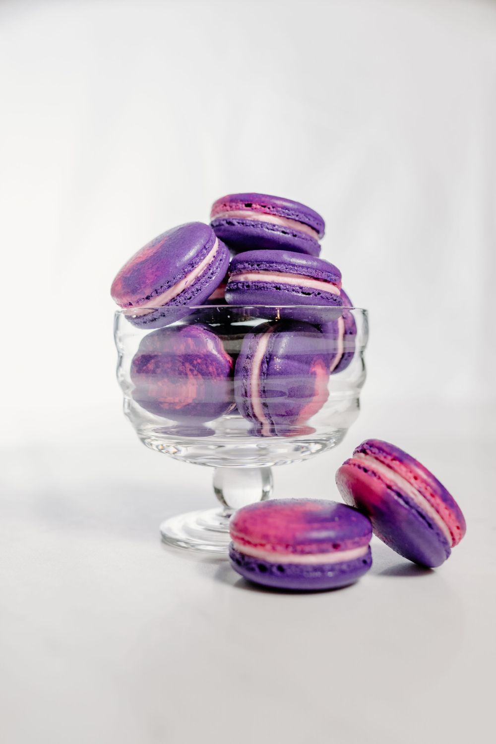 Vibrant purple and pink macarons displayed in an elegant glass dessert stand.