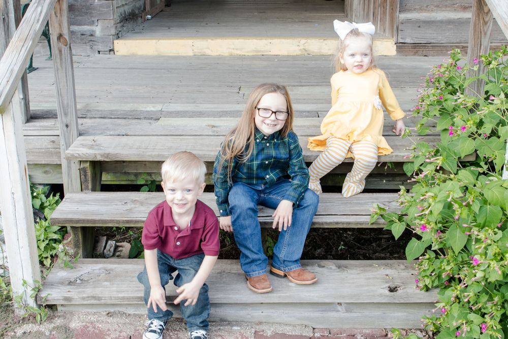 Three children sitting on wooden porch steps outdoors.