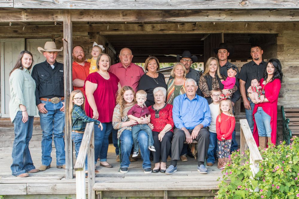 Extended family wearing red and blue poses together on vintage farmhouse porch.