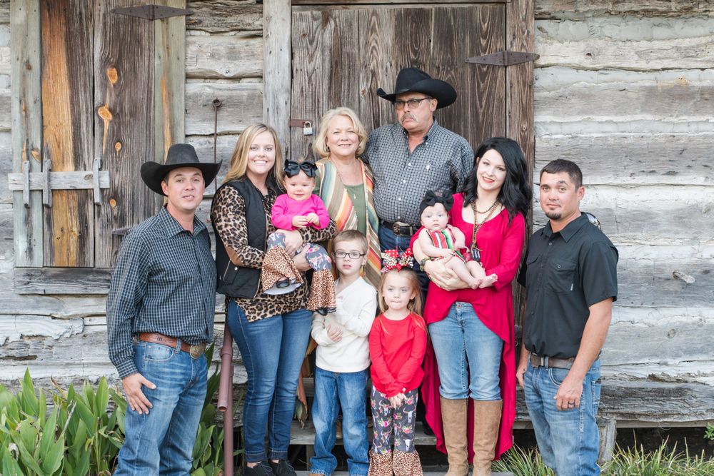 Family group in western attire poses against weathered log cabin wall.