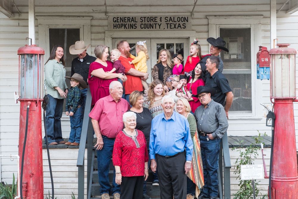 Large group gathered on steps of historic general store with red posts.