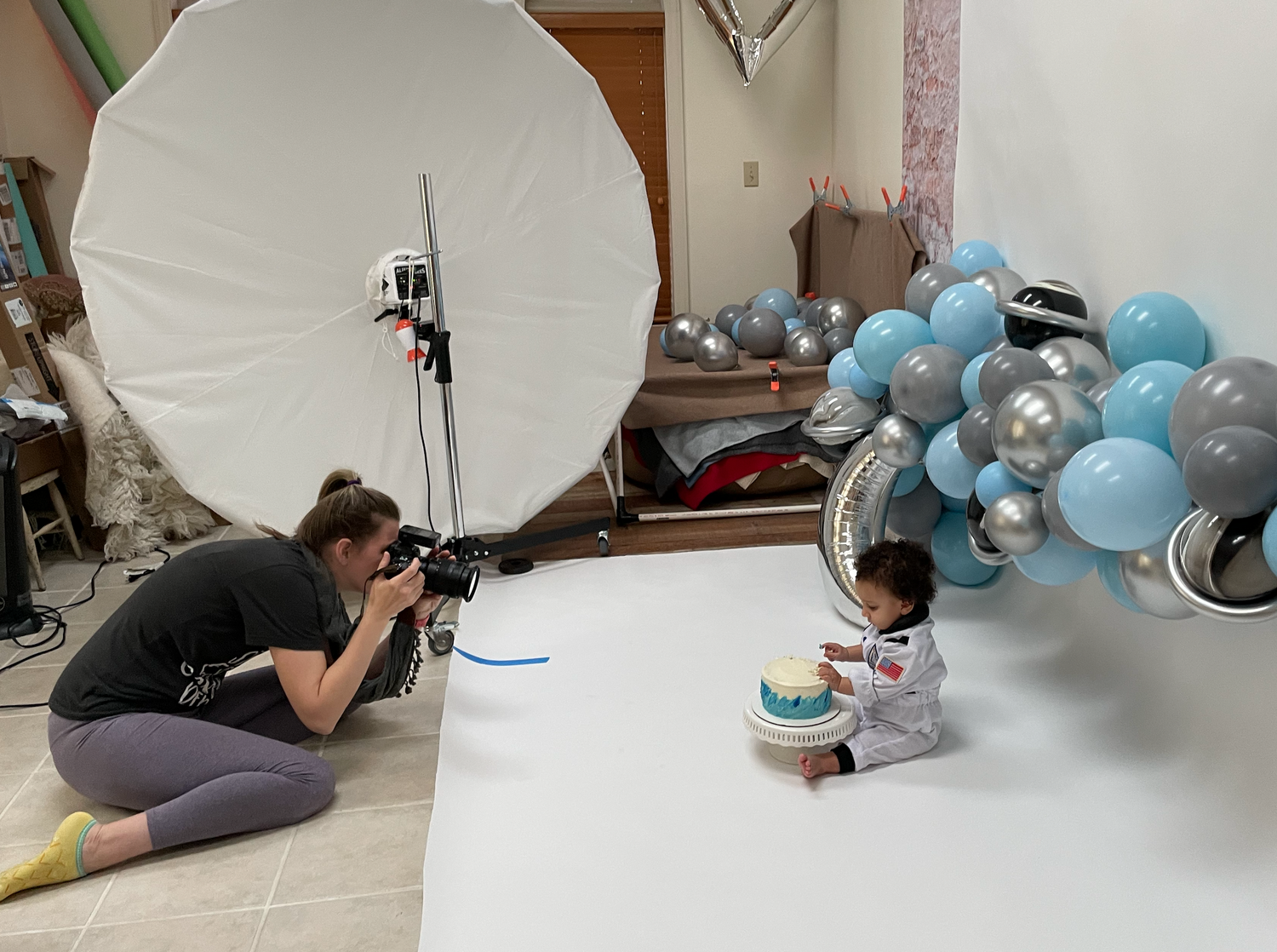 Photography setup with white umbrella light and blue balloons for baby photoshoot.