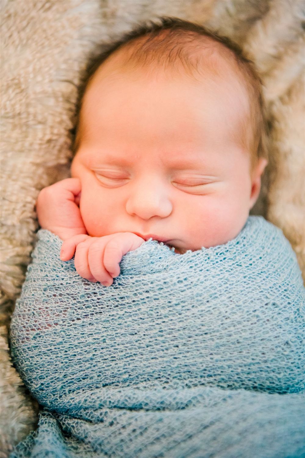 Peaceful newborn baby sleeping wrapped in soft blue knit blanket.