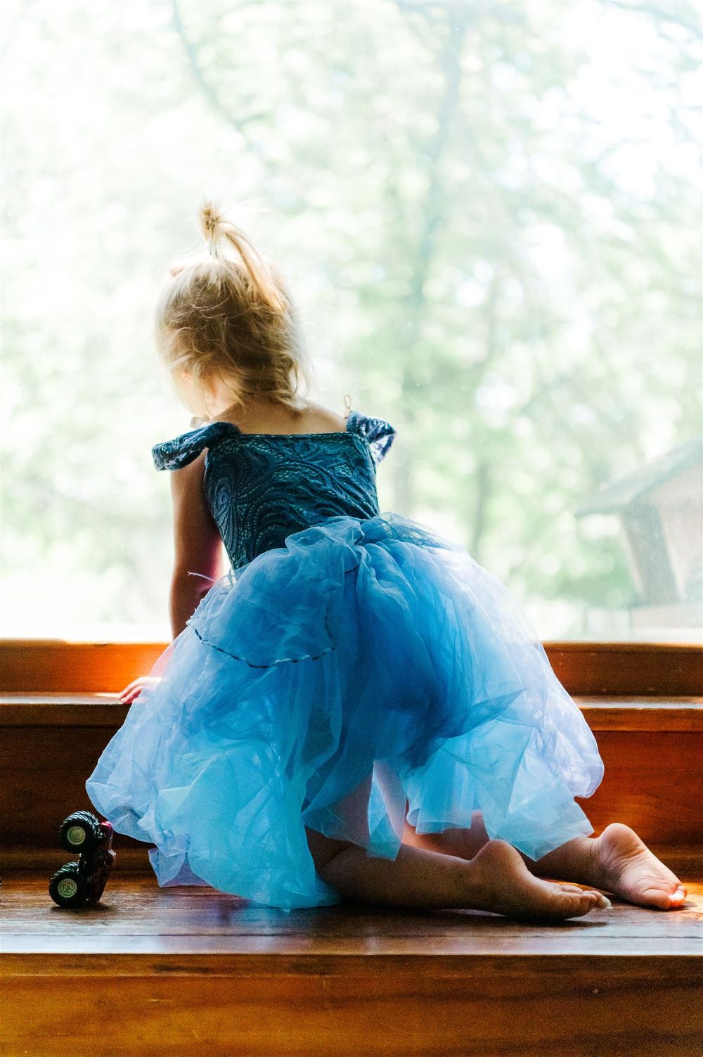 Child in blue tulle dress sitting by window in dreamy pose.