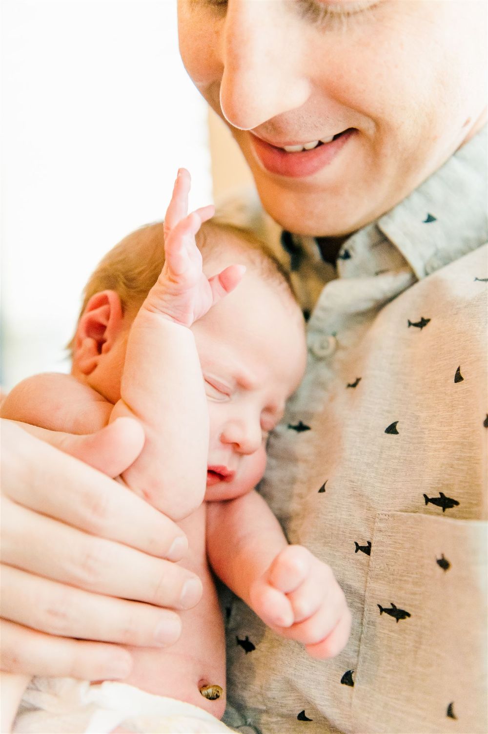 Parent holding sleeping newborn baby against patterned shirt.