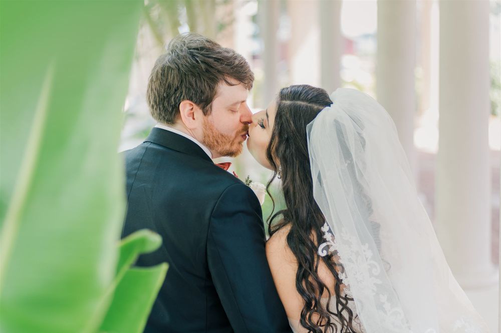 A romantic wedding portrait showing a couple sharing a tender moment near green foliage.