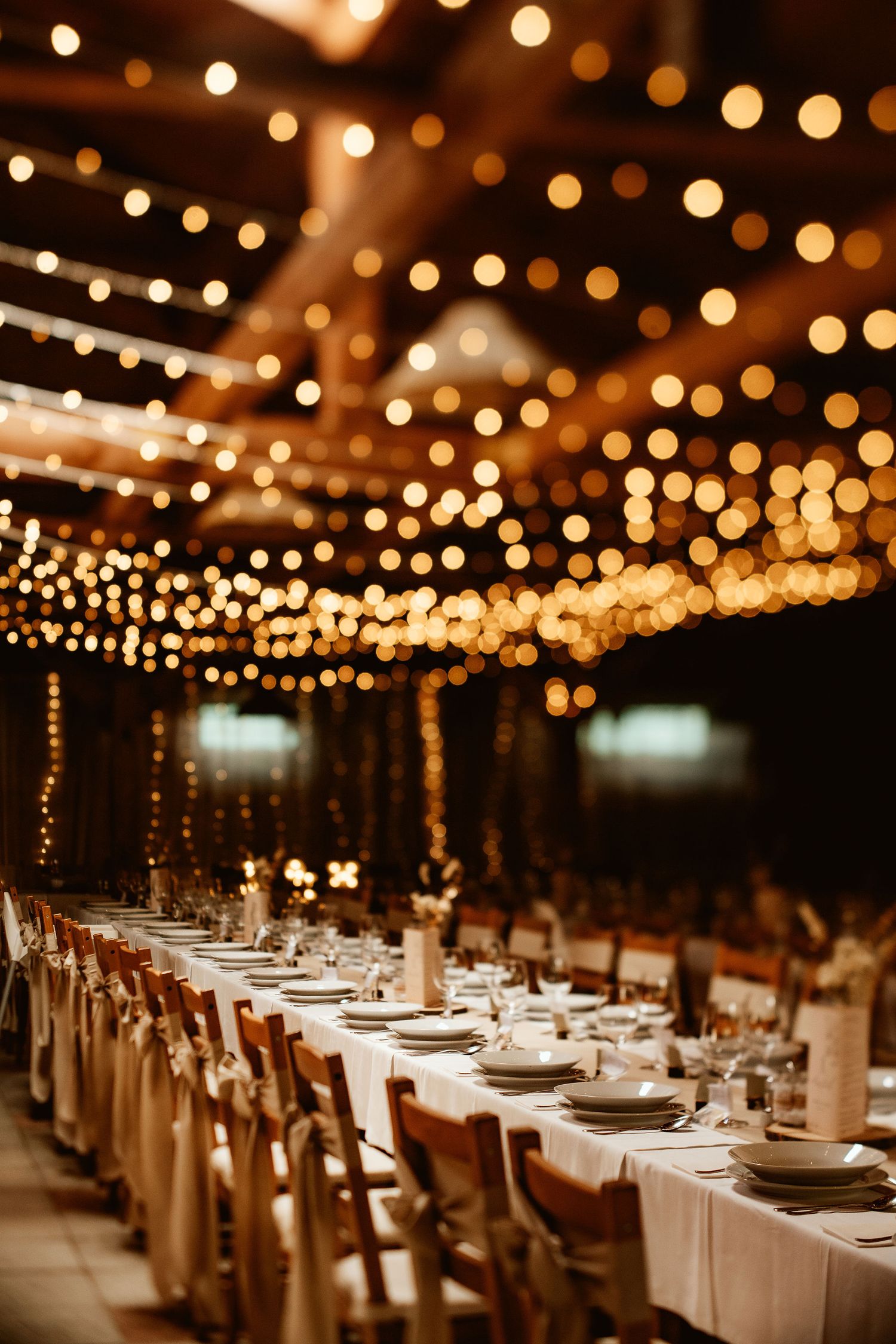 Wedding reception venue with twinkling string lights overhead and long tables set with white linens.