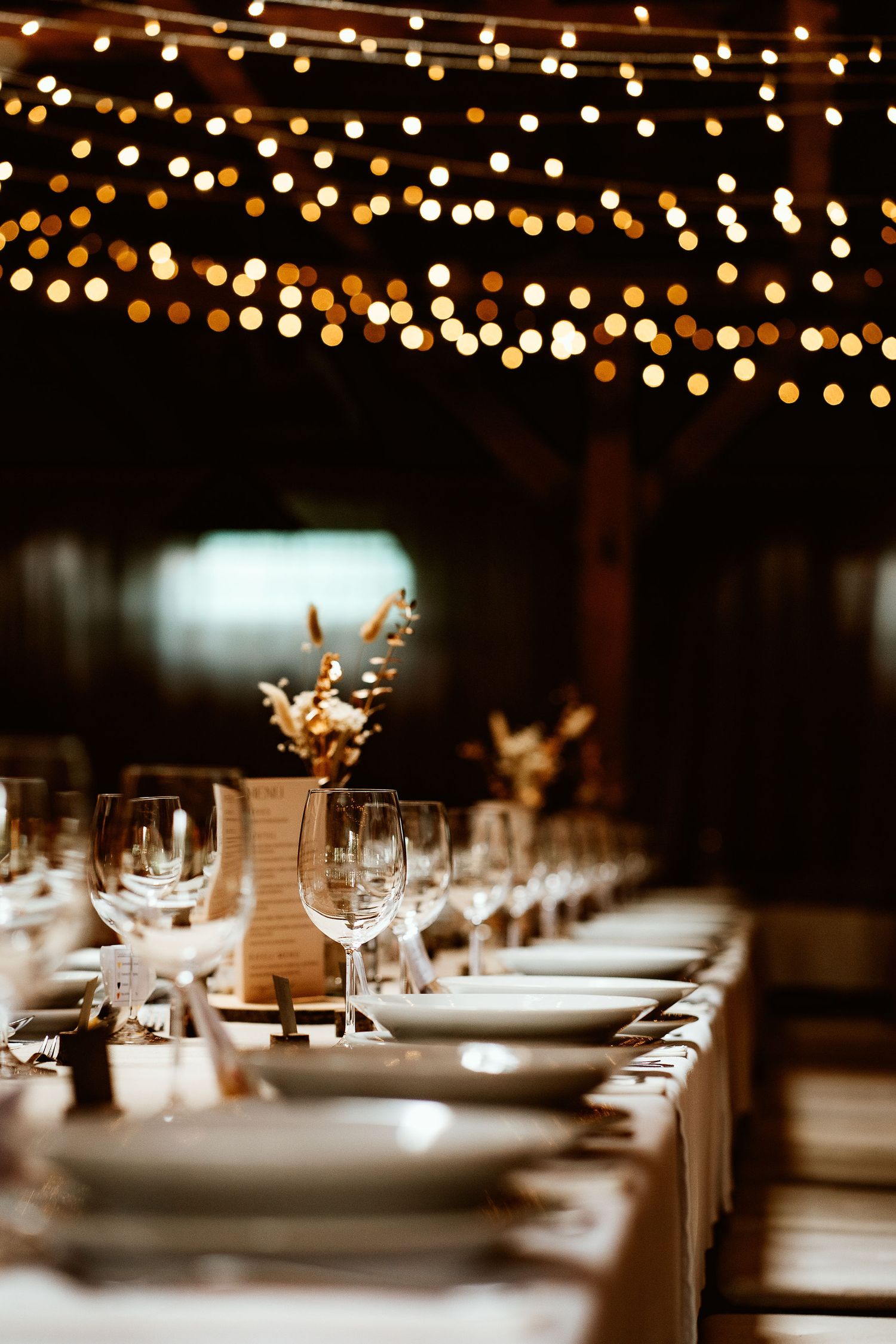 Long banquet table set for a wedding reception with bokeh lights and delicate floral centerpieces.