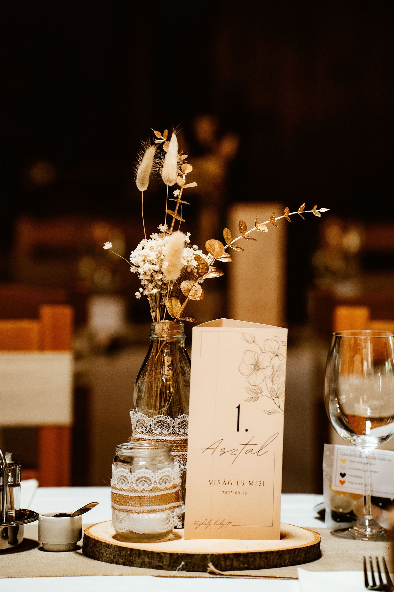 Rustic wedding table centerpiece featuring dried flowers, lace details and menu card on wooden slice.
