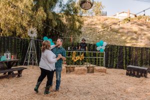 Couple embracing in an outdoor setting with teal balloons and string lights creating a romantic atmosphere.