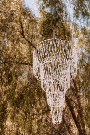 Crystal chandeliers hanging outdoors with willow trees in the background.