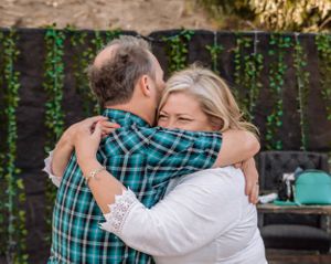 Emotional embrace captured in outdoor setting with decorative lights and greenery.