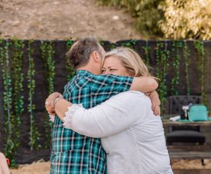 Couple sharing emotional embrace in garden setting with string lights and decorative elements.